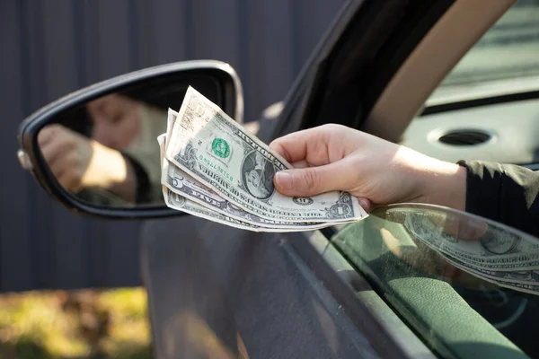 a woman\'s hand pulls out a dellara from a car window, corruption and bribes on the road