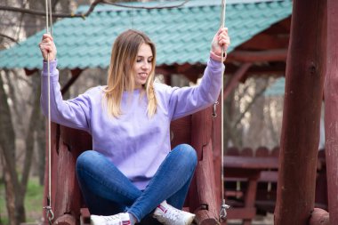 Dnipro şehrinde, Ukrayna 'da bir bahar parkında, tahta salıncakta oturan bir kız.