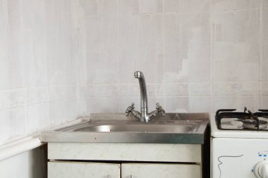 Mutfaktaki eski lavabo ve musluk beyaz fayansların arka planına yakın plan.