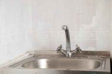 Mutfaktaki eski lavabo ve musluk beyaz fayansların arka planına yakın plan.