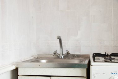 Mutfaktaki eski lavabo ve musluk beyaz fayansların arka planına yakın plan.