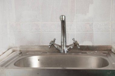 Mutfaktaki eski lavabo ve musluk beyaz fayansların arka planına yakın plan.