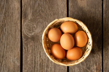 Sarı tavuk yumurtaları hasır bir sepetin içinde eski ahşap bir masanın üzerinde duruyor.