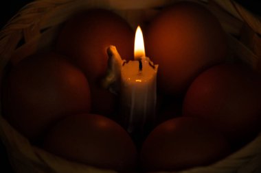 Sarı tavuk yumurtaları ve mum yanan mum hasır bir sepette, karanlıkta, Paskalya bayramında