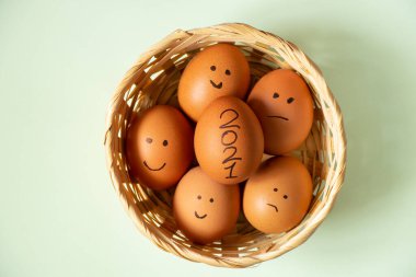 Tavuk yumurtalarına boyanmış yüz ifadeleri ve yalıtılmış arka planda hasır bir sepetin içinde yatan 2021.