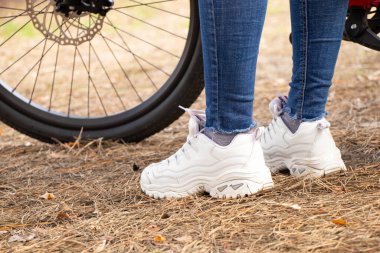 Parktaki bisikletin yanında beyaz deri ayakkabılı kadın bacakları dinleniyor.