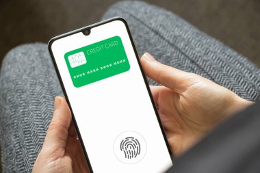 Beyaz ekran ve yeşil kredi kartıyla telefonu tutan kadın elleri, telefon aracılığıyla online ödeme