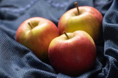 Olgun kırmızı elmalar koyu mavi bir kumaşın üzerinde uzanıyorlar.