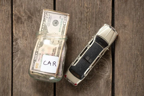 glass jar with dollars and a toy car on an old wooden table, save money for a car, money in the bank