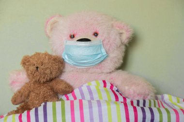 Yatakta oturan oyuncak ayının üstündeki tıbbi maske, çocuklar hastalanır, hastalanır.