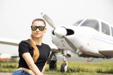 young beautiful girl sits on the grass on the background of a small plane in Ukraine in the spring, rest travel