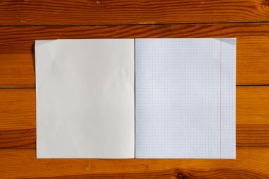 a blank school notebook in a cage lies on a wooden desk close-up, space for text