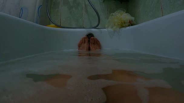 Kobiece stopy w pełnej wannie z mydlaną wodą, dziewczyna w łazience myje się — Wideo stockowe