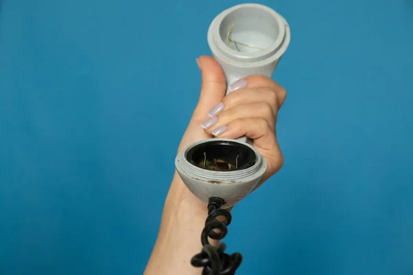 female hand holding an old broken telephone receiver on a wire on a blue isolated background, the telephone receiver on the prododi is broken