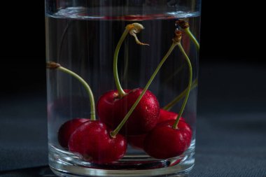 Masadaki siyah arka planda bir bardak suyun içindeki kirazlar, meyve arka planı, meyveler.