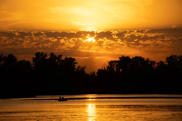 Gün batımında bir teknede balıkçı Ukrayna ormanının arka planında Dinyeper şehrinde, Dinyeper nehrinde altın gün batımında.