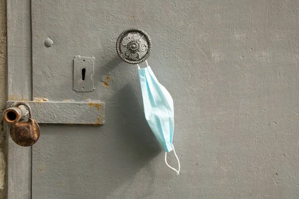 a medical mask hangs on the handle on an old iron rusty door on the street at the house, stop quarantined