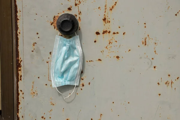 a medical mask hangs on the handle on an old iron rusty door on the street at the house, stop quarantined