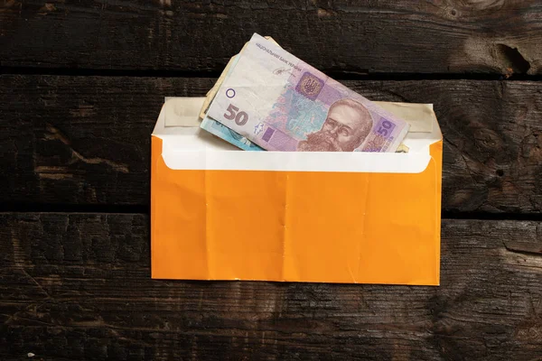 Tahta bir masanın üzerinde sarı bir zarf içinde Ukrayna Hrivnia 'sı, ücretler bir zarfın içinde, para bir zarfın içinde.