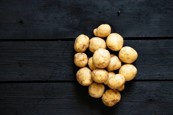 young raw potatoes lie on a black wooden table, potatoes on a wooden background