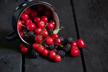 Siyah ahşap bir masada, meyve arka planında, meyve suyunda, kiraz ve dut.