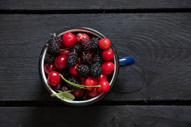 Siyah ahşap bir masada, meyve arka planında, meyve suyunda, kiraz ve dut.