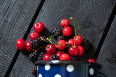 Siyah ahşap bir masada, meyve arka planında, meyve suyunda, kiraz ve dut.