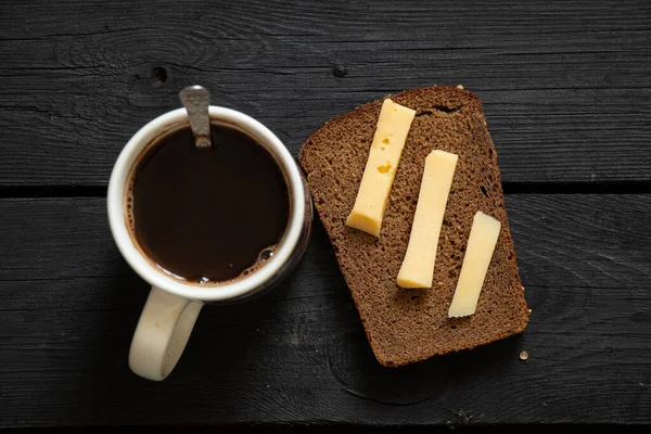 a cup with black coffee and a slice of bread with hard cheese on a black wooden table, homemade coffee for breakfast with a sandwich