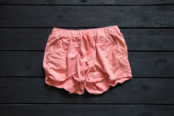 黑色木制背景的粉色短裤 — 图库照片