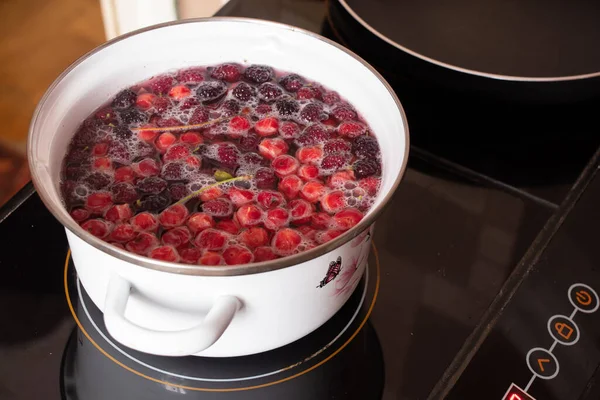 homemade fruit compote with cherry boils on the stove in the kitchen in a white saucepan, fruit compote in a saucepan