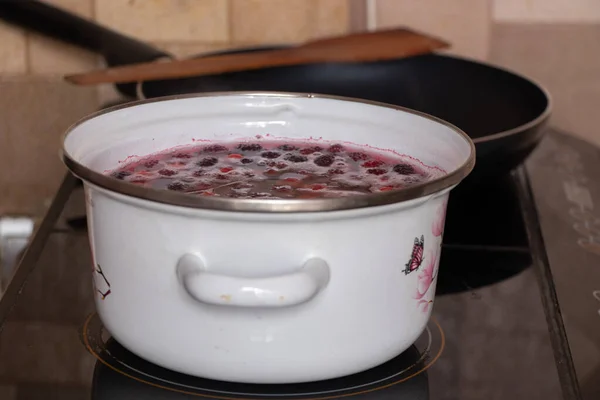homemade fruit compote with cherry boils on the stove in the kitchen in a white saucepan, fruit compote in a saucepan