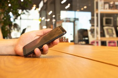 Kafedeki masada oturan bir adamın elinde bir cep telefonu, elinde bir telefon.