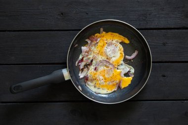 Tavada soğanlı kızarmış tavuk yumurtası siyah ahşap bir masada duruyor, kahvaltıda çırpılmış yumurta.