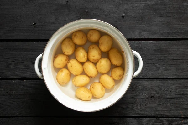 Young Whole Raw Potatoes Water Saucepan Stands Black Wooden Table — Stock Photo, Image