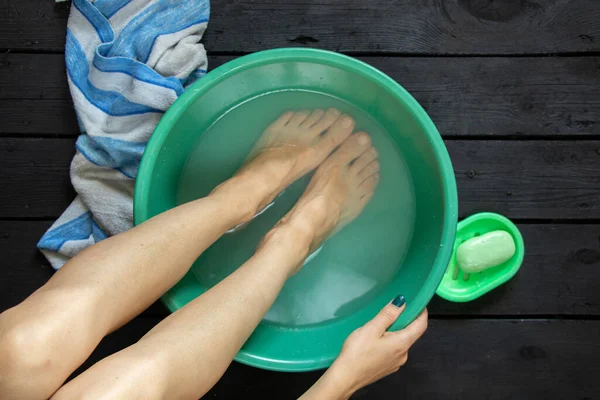 girl washes her feet in a bowl of water on the wooden floor at home, foot care, wash feet at home, hygiene