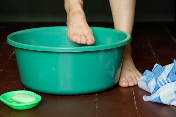 girl washes her feet in a bowl of water on the wooden floor at home, foot care, wash feet at home, hygiene