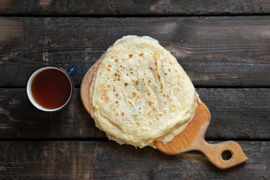 Tahta eski bir masada bir fincan kahvenin yanında krep yığını, kahvaltıda gözleme.