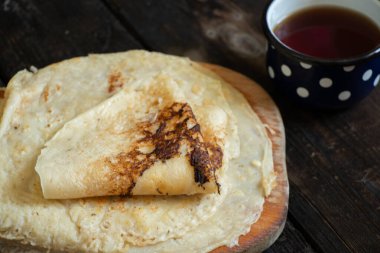 Tahta eski bir masada bir fincan kahvenin yanında krep yığını, kahvaltıda gözleme.