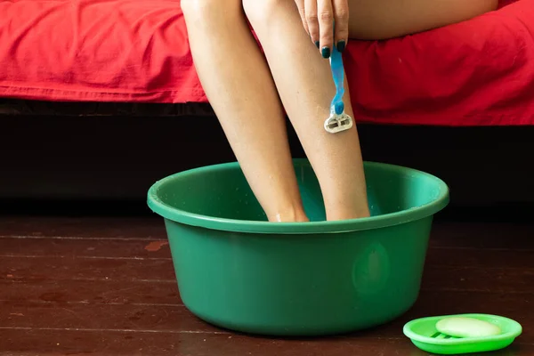 少女は家の木製の床にある緑色のプラスチック製のボウルに足を剃り床にあるボウルに足を洗い — ストック写真