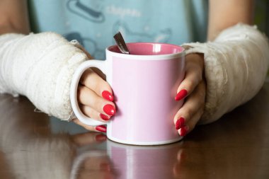 Alçıda iki kolu kırık bir kız kahvaltı için mutfakta bir fincan çay tutuyor, alçıda kırık kollar, kırık uzuvlar, yaralanma.