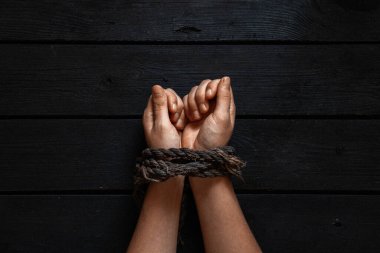 Eski bir iple bağlanmış kadın elleri siyah tahta bir arka planda, elleri bağlı, kölelik