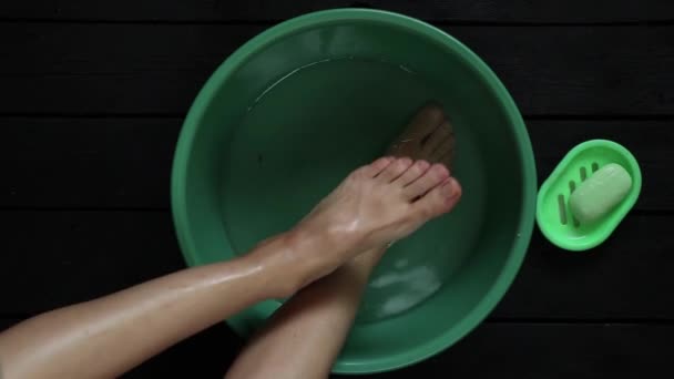 女の子は家の木の床の上の水のボウルに足を洗う 足のケア 自宅で足を洗う — ストック動画