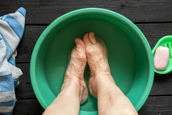 Yaşlı Büyükannenin Ayakları Siyah Zeminde Sabunla Plastik Bir Kasede Yıkanır — Stok fotoğraf