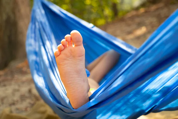 Çocuk ayağı hamakta, yazın güneş altında ormanda yuvarlanıyor, hamakta dinleniyor, hamakta dinleniyor, ormanda dinleniyor.