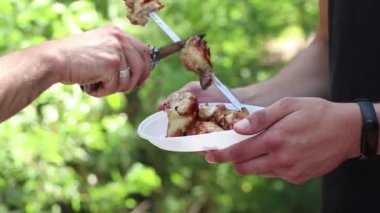 Kızarmış şiş kebap bir adamın ellerinde plastik bir tabağa konacak, açık bir tabakta ateşte kızarmış et, tabakta şiş kebap.