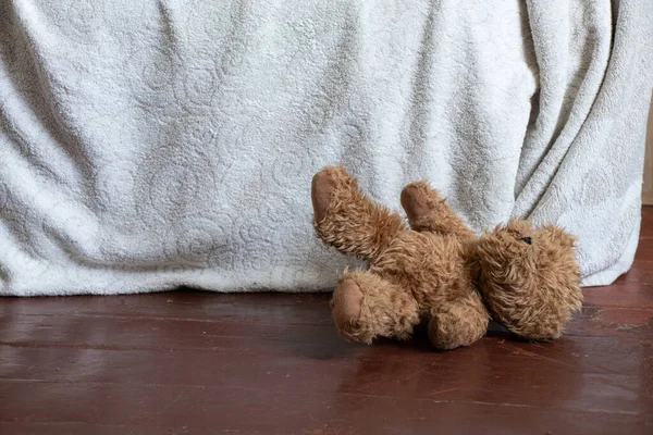 Un orsacchiotto marrone si trova vicino al letto sul pavimento in camera da letto a casa — Foto Stock