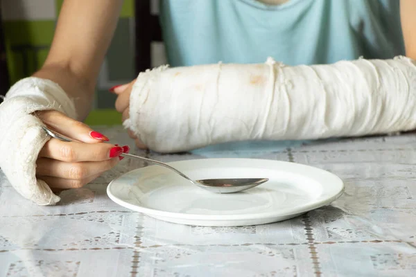 在厨房的饭桌上 一个女孩拿着勺子和盘子一起吃早餐 胳膊被压断了 四肢骨折 — 图库照片
