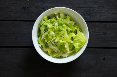 Dilimlenmiş yeşil salata beyaz plastik bir kasede siyah tahta bir masada, yemyeşil salata, sağlıklı yiyecekler.