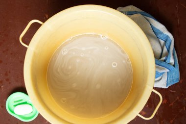 Ayaklarını yıkadıktan sonra sabunlu bir plastik kase yerde sabun ve havlunun yanında, yerde bir kase su var.