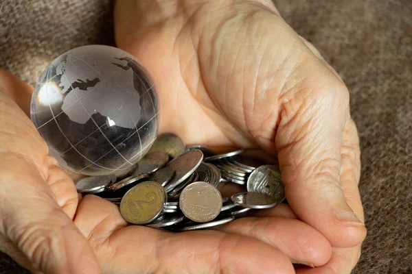 Ukrainian pennies and a glass globe of the planet lies in the hands of an old woman, finance and people